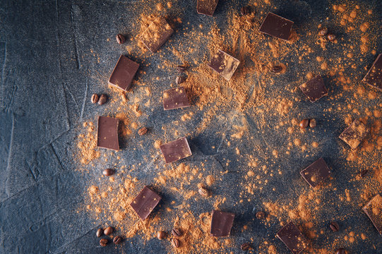 Chocolate bar pieces, cocoa powder and coffee beans on dark stone background. Background with chocolate. Slices of chocolate. Sweet food photo concept. Copyspace.