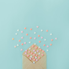 Multicolor sweets sugar candy hearts fly out of craft paper envelope on the light blue background . Valentine day. love concept. Gift, message for lover. Space for text. Square banner.