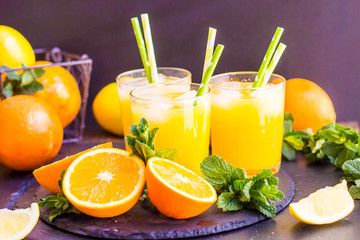 glass jar of fresh orange juice with fresh fruits on dark table.