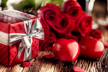 Valentine wedding concept. Bouquet of roses and wrapped gift with red hearts on wooden table