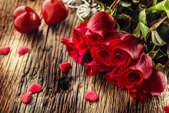 Valentine wedding concept. Bouquet of roses and wrapped gift with red hearts on wooden table