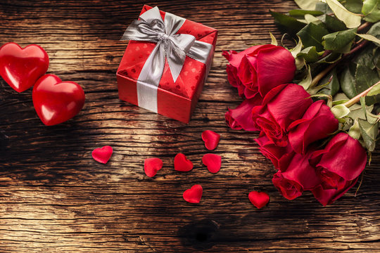 Valentine wedding concept. Bouquet of roses and wrapped gift with red hearts on wooden table