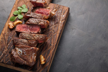 Closeup ready to eat steak new York beef breeds of black Angus with herbs, garlic and butter on a wooden Board. The finished dish for dinner on a dark stone background. Top view with copy space