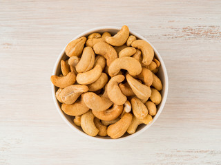 white bowl with a handful of nuts of cashew on white background table, top view