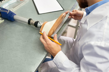 Close up of unrecognizable prosthetist measuring artificial foot while working at table in design laboratory