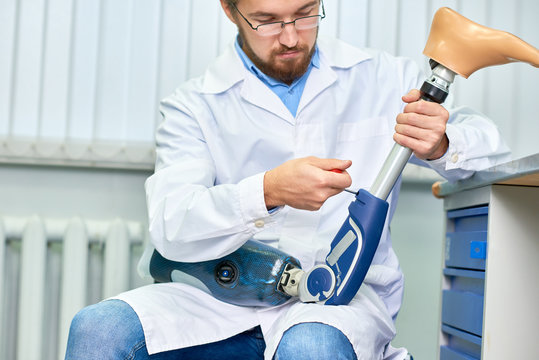 Portrait of bearded technician checking artificial limb while sitting at desk in office, adjusting it and checking for quality