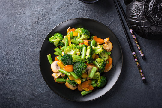 Hot stir fried vegetables on black plate. Healthy asian food concept with copy space.