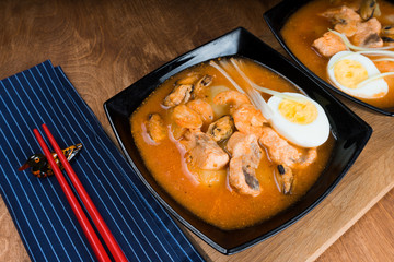 Soup with shrimps in bowl with tomatoes and herbs on wooden table.