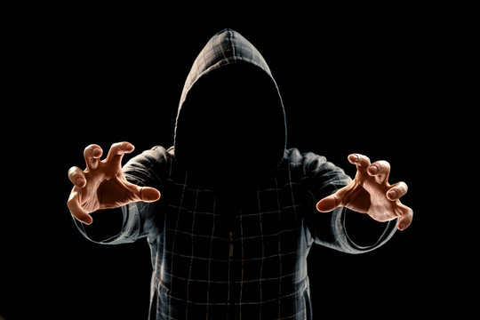 Portrait, silhouette of a man in a hood on a black background, his face is not visible. The concept of a criminal, incognito, mystery, secrecy, anonymity.