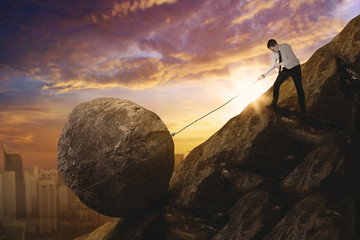 Caucasian businessman pulling a rock on the cliff