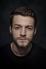 Portrait of a young man with a beard on a dark background.