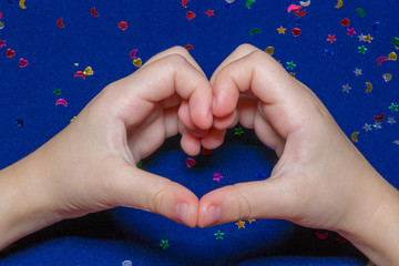 Two hands making heart around a sparkling heats and stars on blue background