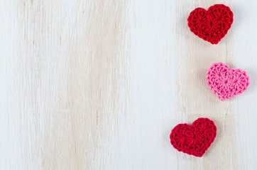 Knitted red hearts on a white wooden background