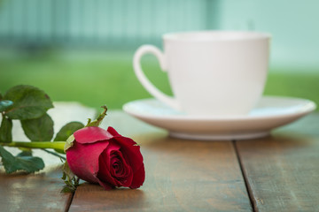 Cute little white cup of coffee with red rose flower on wooden table and home garden background. Romantic table setting, Valentine day celebration, Love concept, Positive thinking concept.