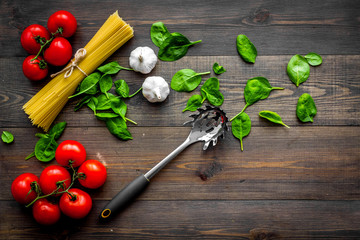 Main ingredients for italian pasta. Spaghetti, tomatoes, garlic, green basil on dark wooden background top view copy space
