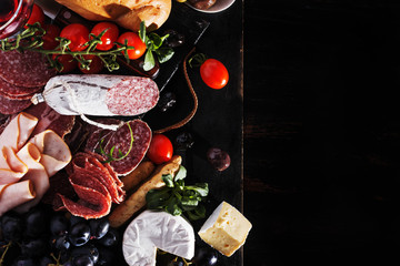 Italian food ingredients ham, salami, tomino, various olives, bread on black wooden board, copy...