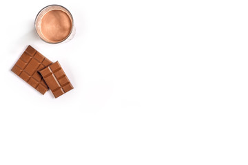 Glass of chocolate milk with chocolate bar on white background with space for text or design. Top view