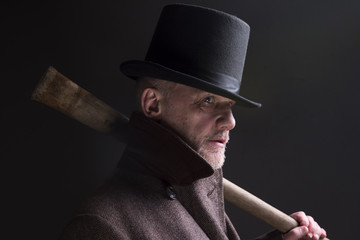 Portrait of a mature man dressed as a sinister Victorian criminal, holding a wooden bat