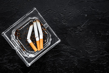Smoking. Half-smoked cigarettes in ashtray on black background top view copy space