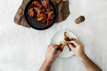 Man eats chicken wings, top view. Dinner table concept