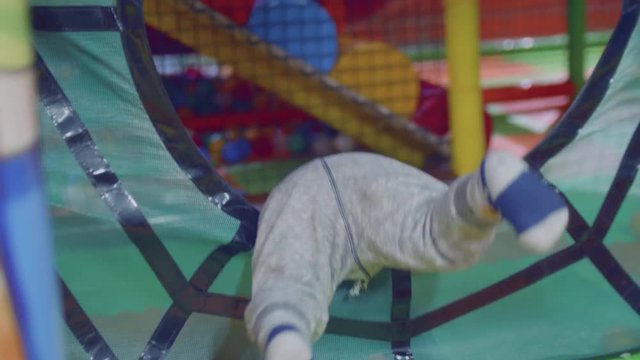 Blond toddler tries to get through toy fence. Back view