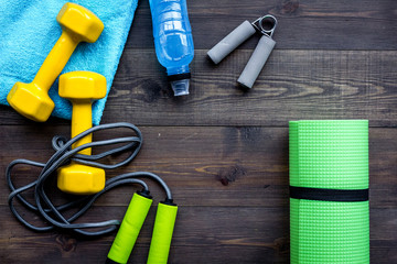 Fitness equipment. Jump rope, dumbbells, expander, mat, water on dark wooden background top view copy space