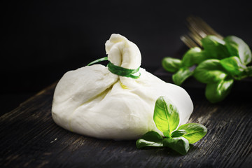 Burrata with basil on black background.