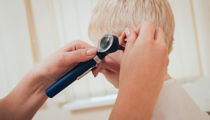 Doctor examines ear with otoscope in a pediatrician room.
