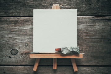 Canvas on easel, paint tube and paintbrush. Old wooden background. Top view. Flat lay. Copy space...