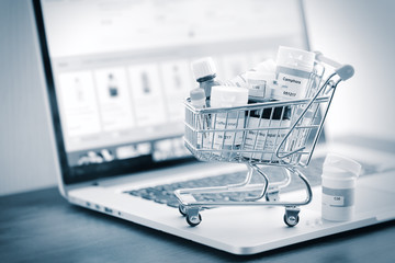 Mini shopping cart full of homeopathic remedies on laptop background. Homeopathy and internet...