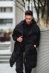 Fashionable man stand on the street near buildings. Winter, autumn outfit. Jacket with blouse and white sneakers.