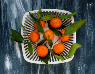 mandarins with green leaves in a white authentic vase for fruit on a blue background