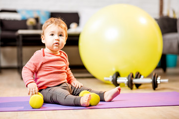 Portrait of a baby boy sitting on the mat with dumbbells and fitness ball at home