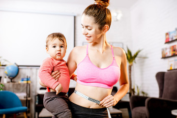 Young mother in sportswear measuring her waist worried about her weight after the child birth...