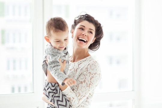 Mother and son playing in a white room. Cute child boy with his mom in white clothes. Happy and lovely Family, communicate with kid