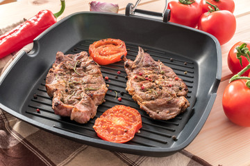 Grilled steak on grill pan with tomatoes on wooden background