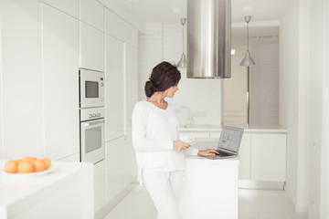 Young real beautiful woman planning expenses and paying bills on her white modern kitchen with laptop.