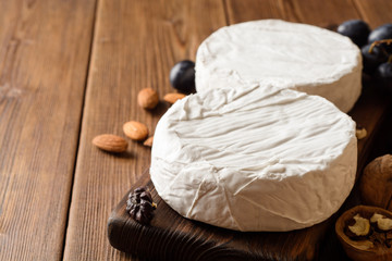 Camembert and brie cheese on wooden cutting board with grape and nuts.