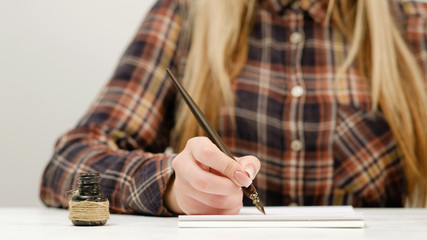 Woman sitting at the table and practicing calligraphy, ink pot beside her. Art of elegant writing