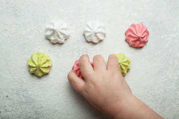 Multicolored meringue air desserts on a white vintage background, joy and celebration. A child's hand takes sweets.