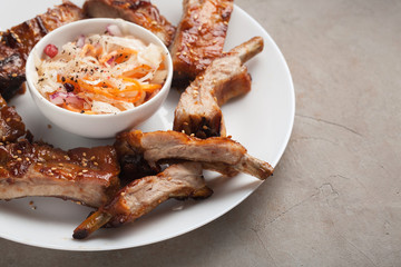 Grilled pork ribs in barbecue sauce and honey with sauerkraut on white plate. Snack to beer on a light stone table