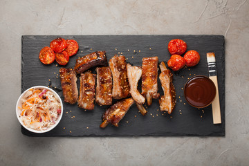 Grilled pork ribs in barbecue sauce and honey with sauerkraut and roasted tomatoes on a black stone Board. Snack to beer on a light stone background. Top view