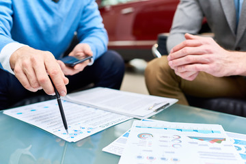 Close up of two unrecognizable young men discussing sales strategies and marketing statistics sitting at coffee table with charts and graphs