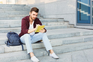 Young student making notes sitting on stairs