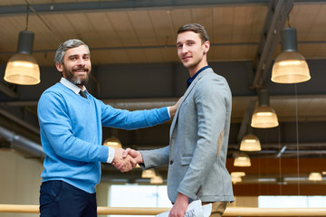 Obraz premium Waist up portrait of two successful business partners shaking hands looking at camera after closing important business deal against background of office building interior, copy space