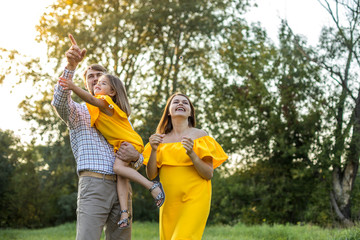 Happy young family with one child having fun together. concept - father, mother and child daughter having fun and playing in nature. yellow clothes. summer sunny day. in green nature together rest