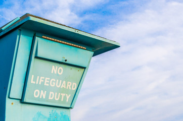 weathered sign saying 'No Lifeguard On Duty' on a lifeguard platform at a beach in Santa Barbara,...