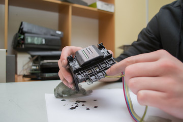 The repair specialist keeps a broken printhead from the inkjet printer in the hands stained. Repair...