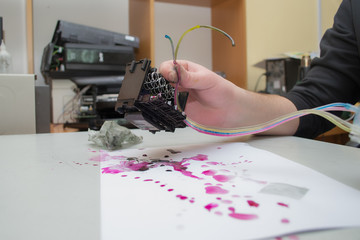 The repair specialist keeps a broken printhead from the inkjet printer in the hands stained. Repair...