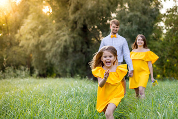 joyful little girl runs along the grass. Behind her go her parents and hold hands. The concept of the family